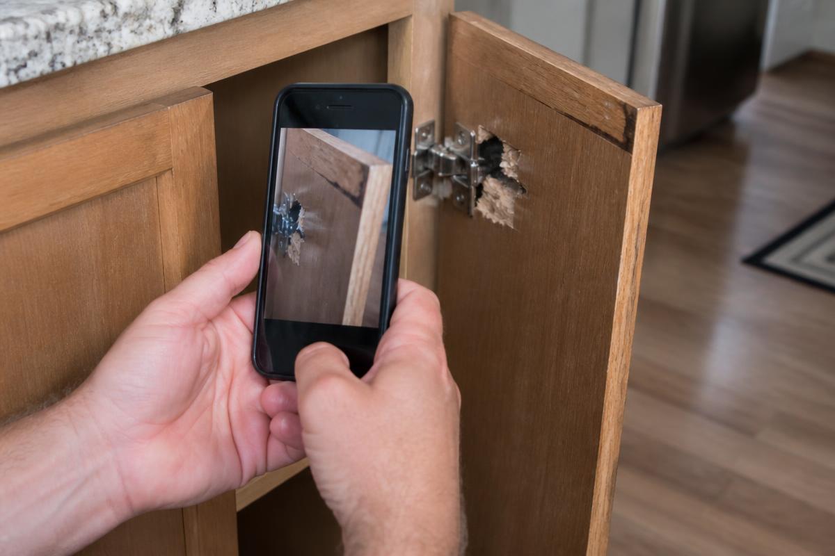 Homeowner photographing a damaged kitchen cabinet hinge with a smartphone